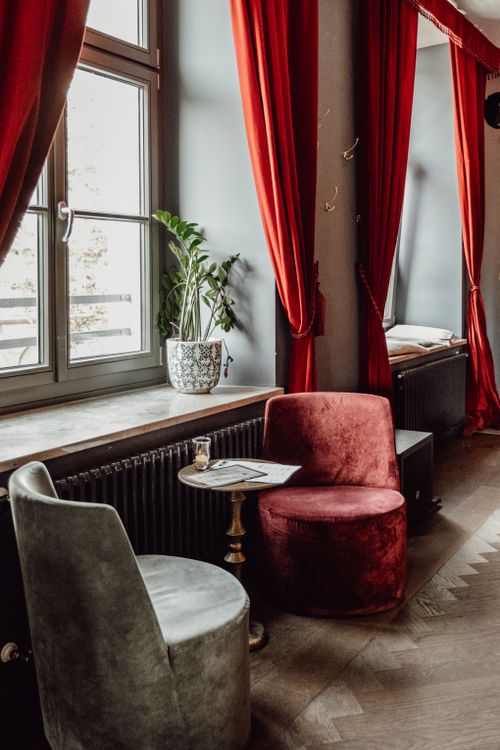 Free Elegant interior of a Munich café featuring velvet armchairs and red curtains next to large windows. Stock Photo