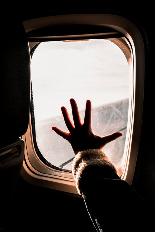 Free A dramatic silhouette of a hand reaching towards an airplane window, evoking a sense of travel and adventure. Stock Photo