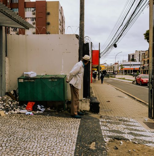 Free A man in a fedora leans against bins on a textured urban street corner. Stock Photo