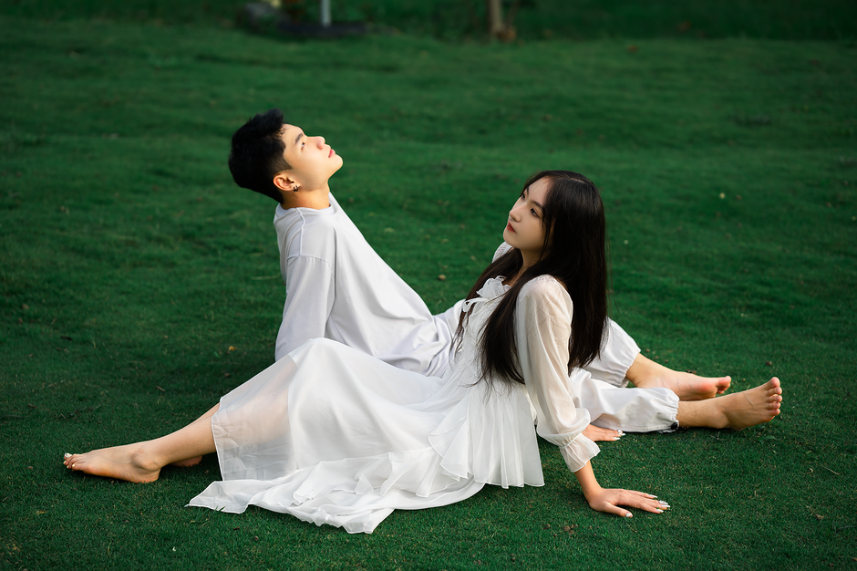 A couple in white outfits relaxing together outdoors on lush green grass in Dalat, Vietnam.