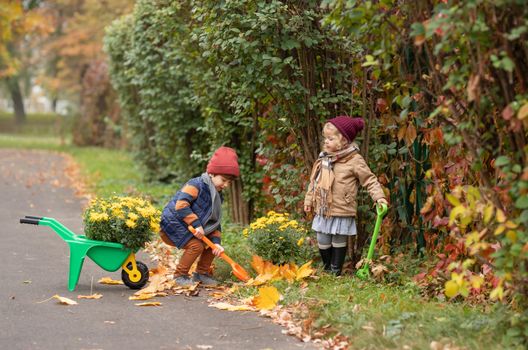 Two children enjoy a playful gardening session in a park filled with autumn colors.