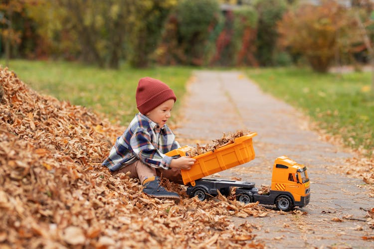 Boy Sitting On Leaves And Playing With Toy Truck