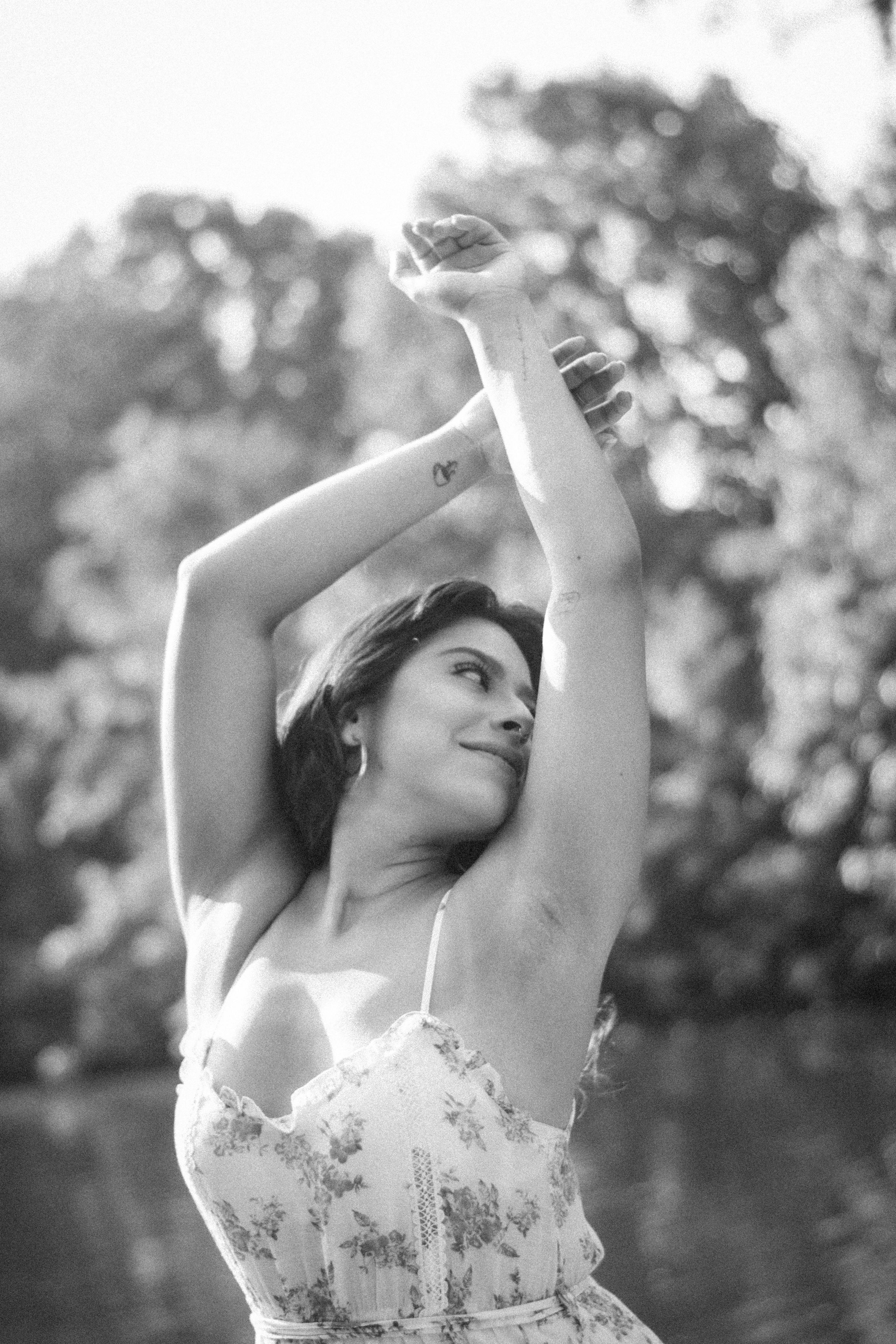 Elegant woman in floral summer dress posing outdoors with arms raised.