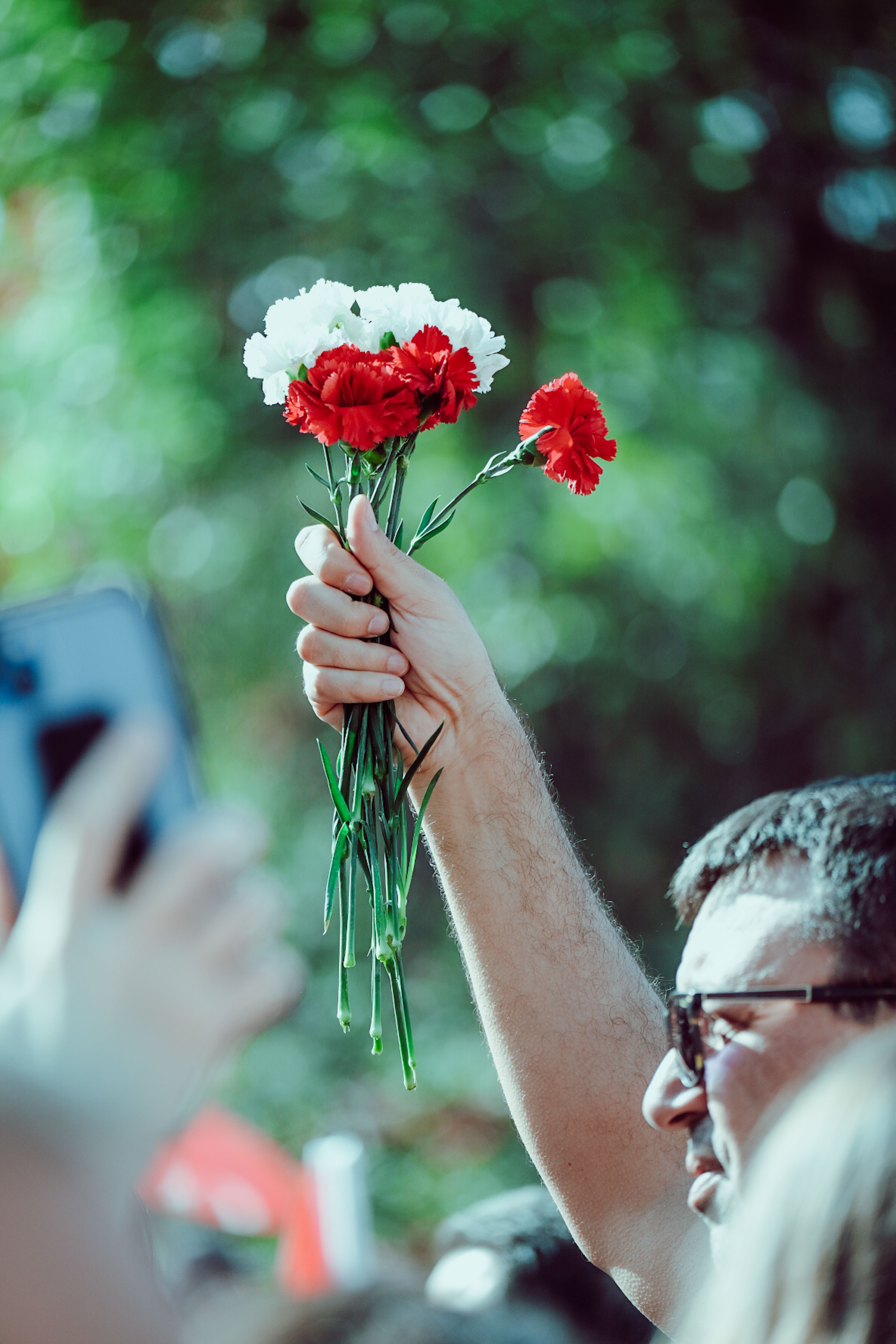 A man raises red and white carnations in a vibrant, lively outdoor setting.