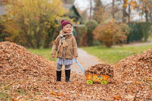 Girl in Jacket Standing with Toy Truck on Leaves in Autumn