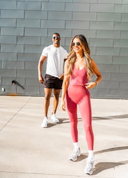 A stylish couple poses confidently in sporty fashion wear under bright sunlight.