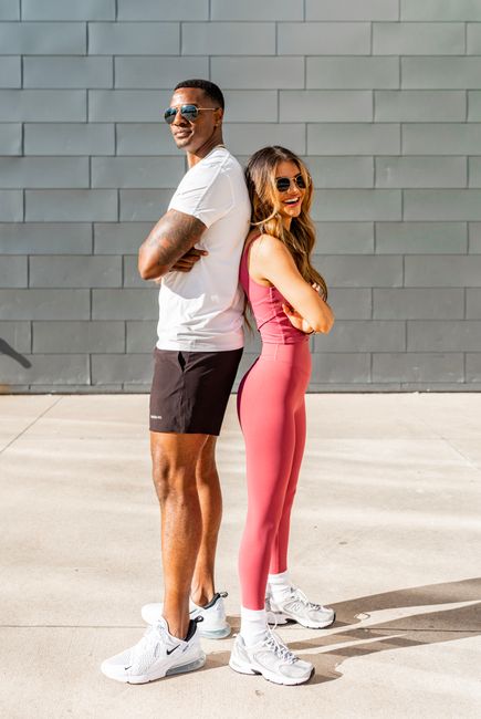 Couple standing back-to-back in trendy sportswear, smiling in an urban setting.