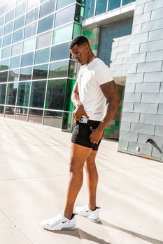 Man in sportswear standing outdoors in front of modern building facade on a sunny day.