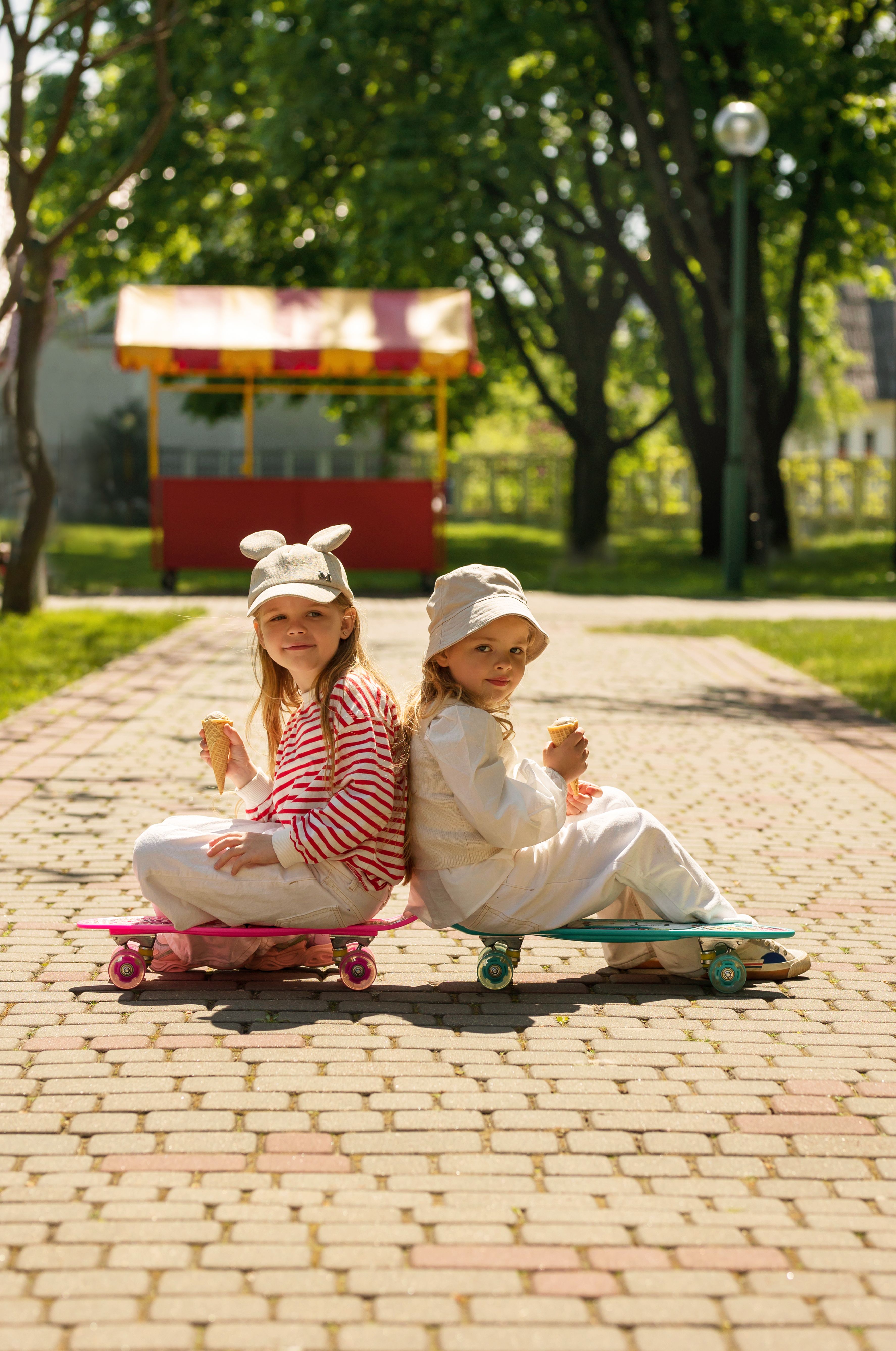 Two girls enjoying ice cream while seated on skateboards in a sunny park.