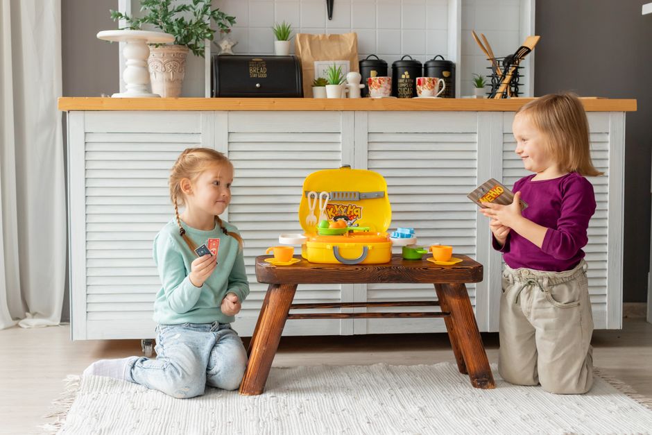 Two young children having fun with toys on a small wooden table indoors. Bright, cheerful, imaginative playtime.