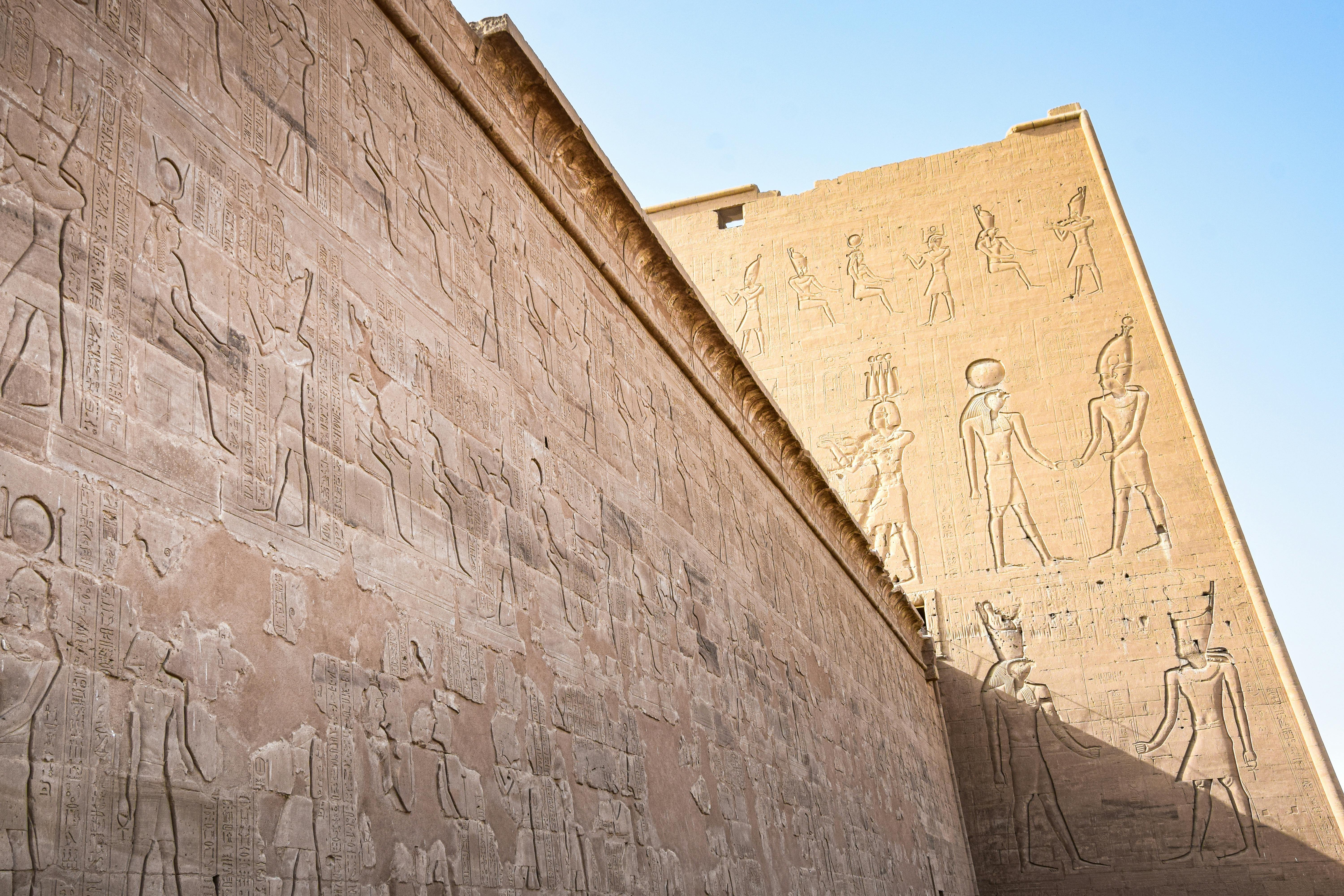 Detailed view of ancient Egyptian temple walls featuring hieroglyphs and historical depictions under clear blue skies.