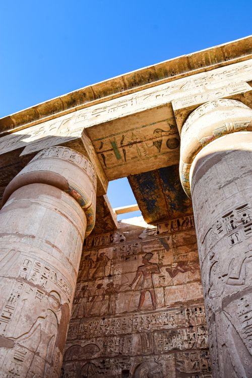 Free Low angle shot of Egyptian temple columns with hieroglyphs under a clear blue sky. Stock Photo