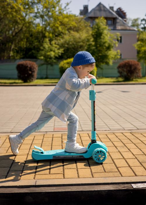 Free Playful child wearing a hat rides a vibrant scooter outdoors on a sunny day. Stock Photo