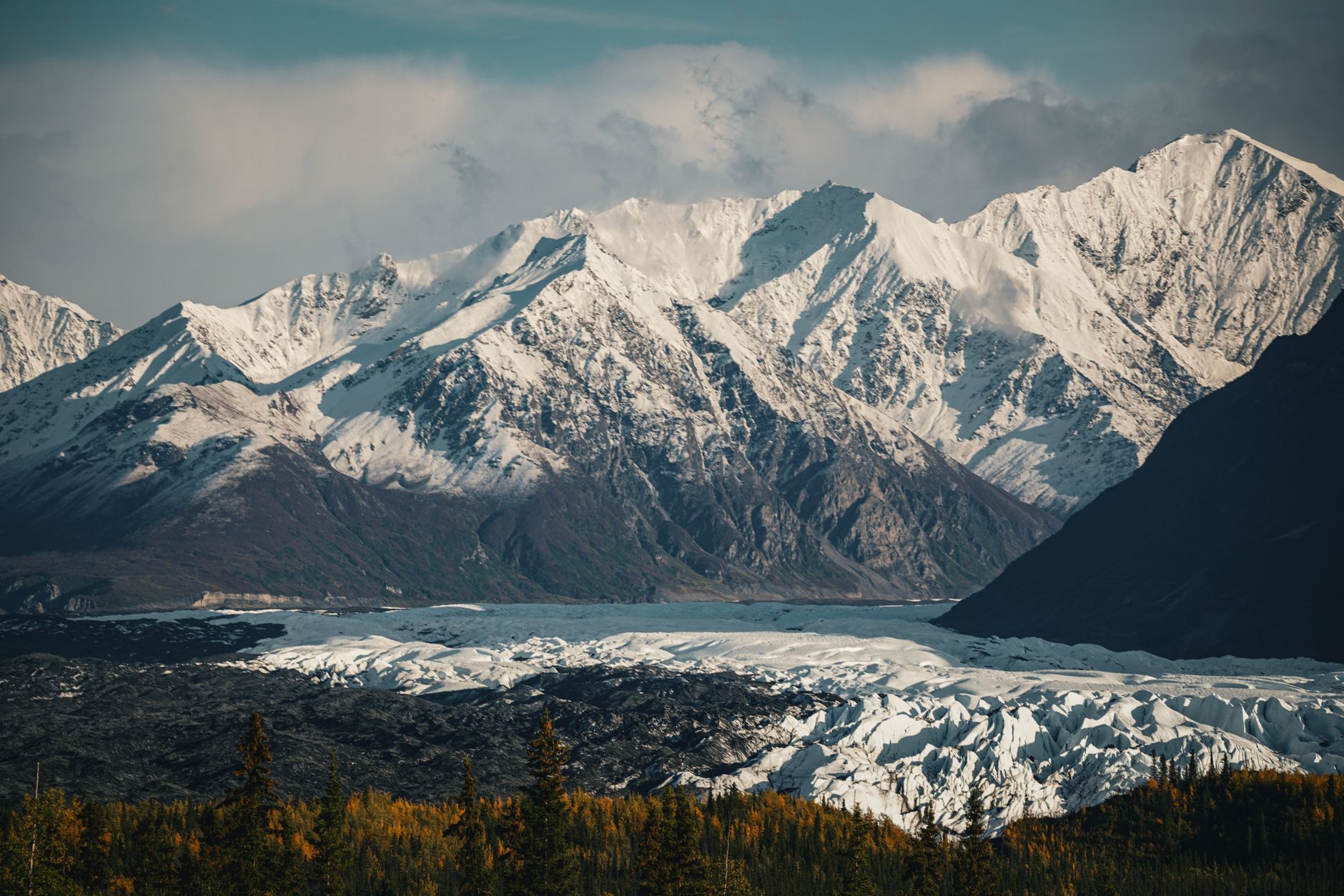 Breathtaking view of snow-capped mountains with a glacier below, captured in serene winter light.