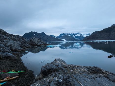 A tranquil lake reflecting majestic snow-capped mountains and kayaks on the shore.