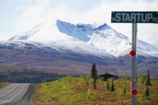 Serene view of a snow-capped mountain with road and rural setting under clear skies.