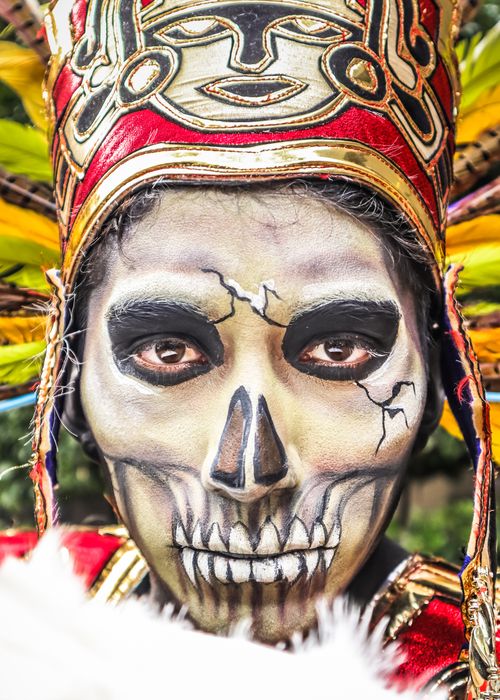 Free Close-up portrait of a person with intricate Aztec-style skull makeup and a colorful headdress. Stock Photo
