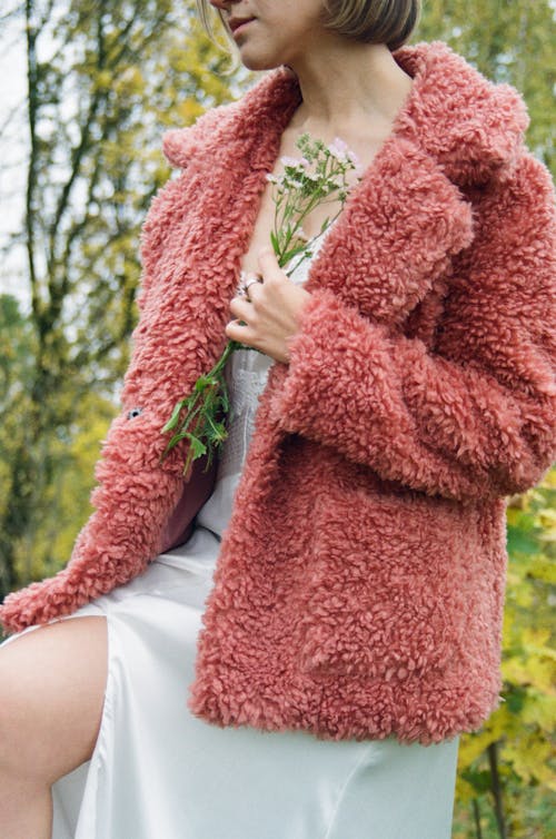 Woman in Pink Fur Coat and White Dress Posing with Flowers in Hand