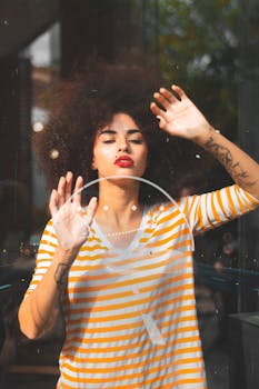 一位留着卷发和纹身的时尚女性在户外玻璃后摆姿势的肖像