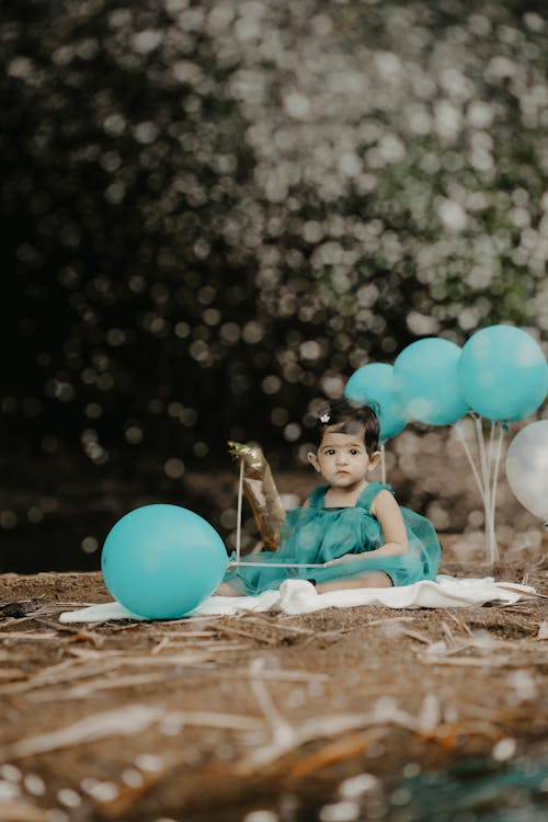 A Little Girl in a Dress Sitting among Birthday Decorations 