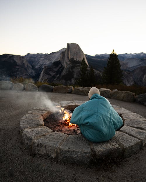 Person in Jacket Sitting by Bonfire in Mountains