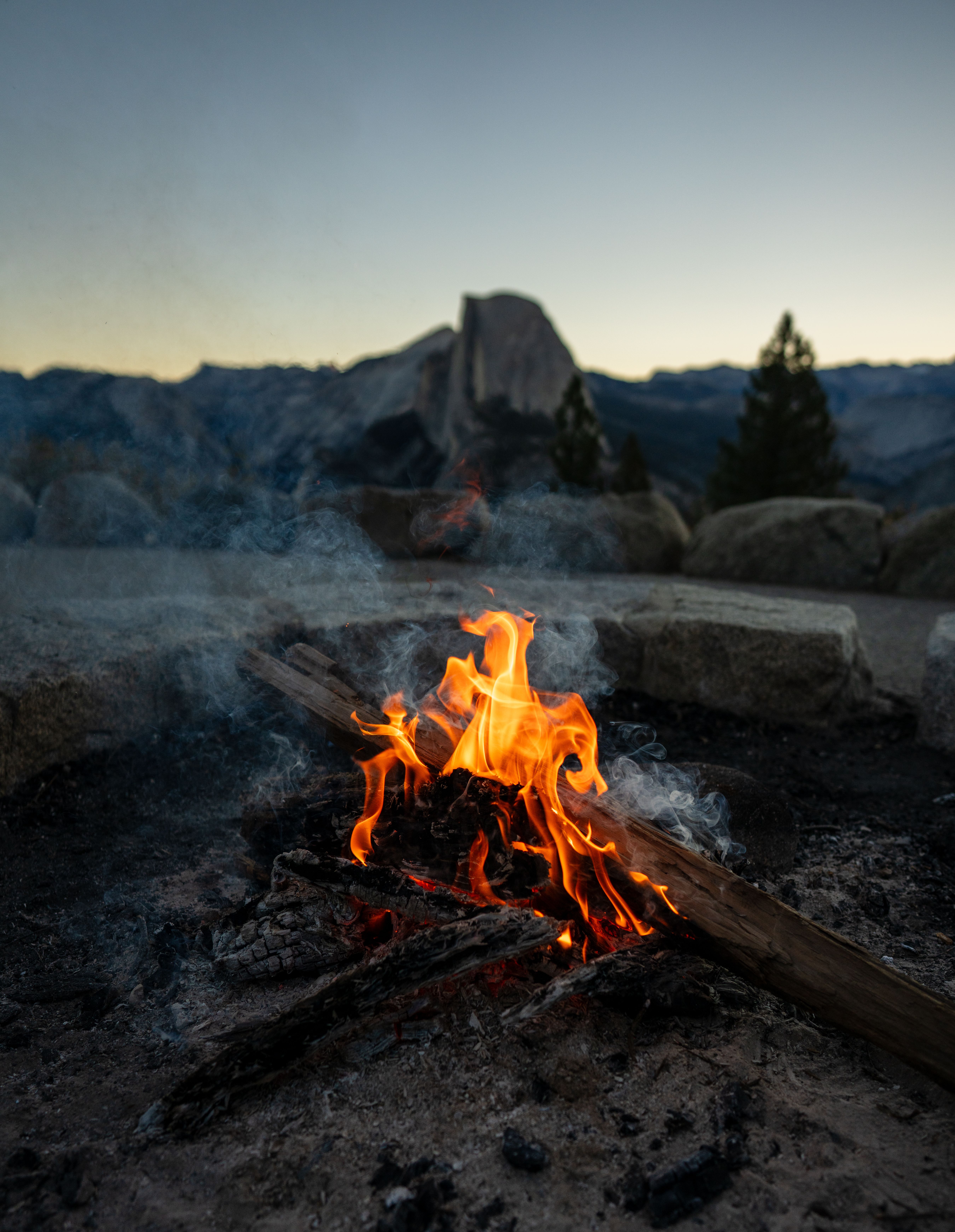 Warm bonfire burning in front of Half Dome at Yosemite during twilight.