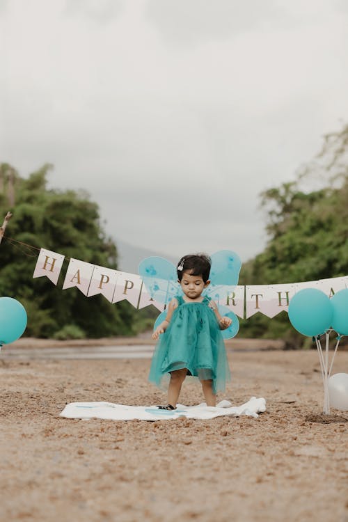 A Little Girl in a Dress Standing among Birthday Decorations 