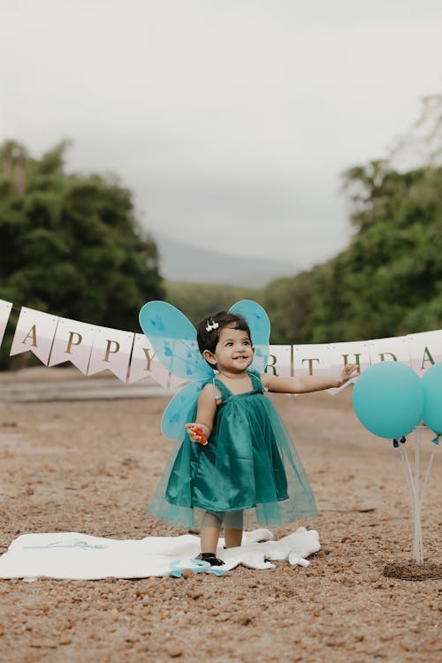 A Little Girl in a Dress Standing among Birthday Decorations 