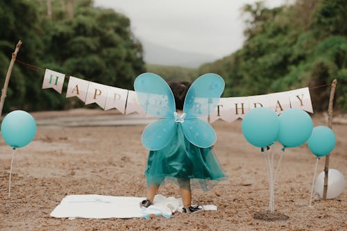 A Little Girl in a Dress Standing among Birthday Decorations 