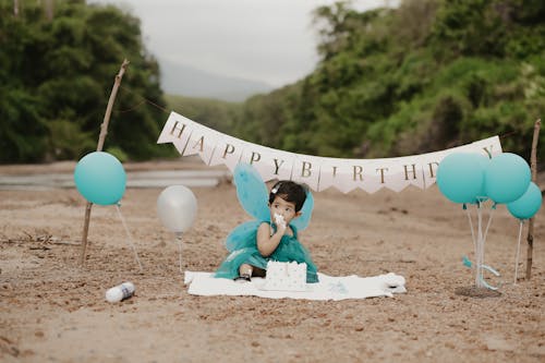 A Little Girl in a Dress Sitting with a Birthday Cake and Balloons 