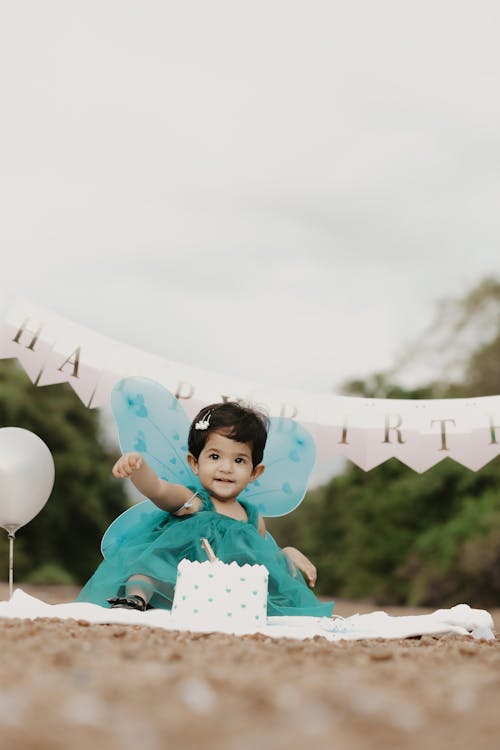 A Little Girl in a Dress Sitting with a Birthday Cake and Balloons 