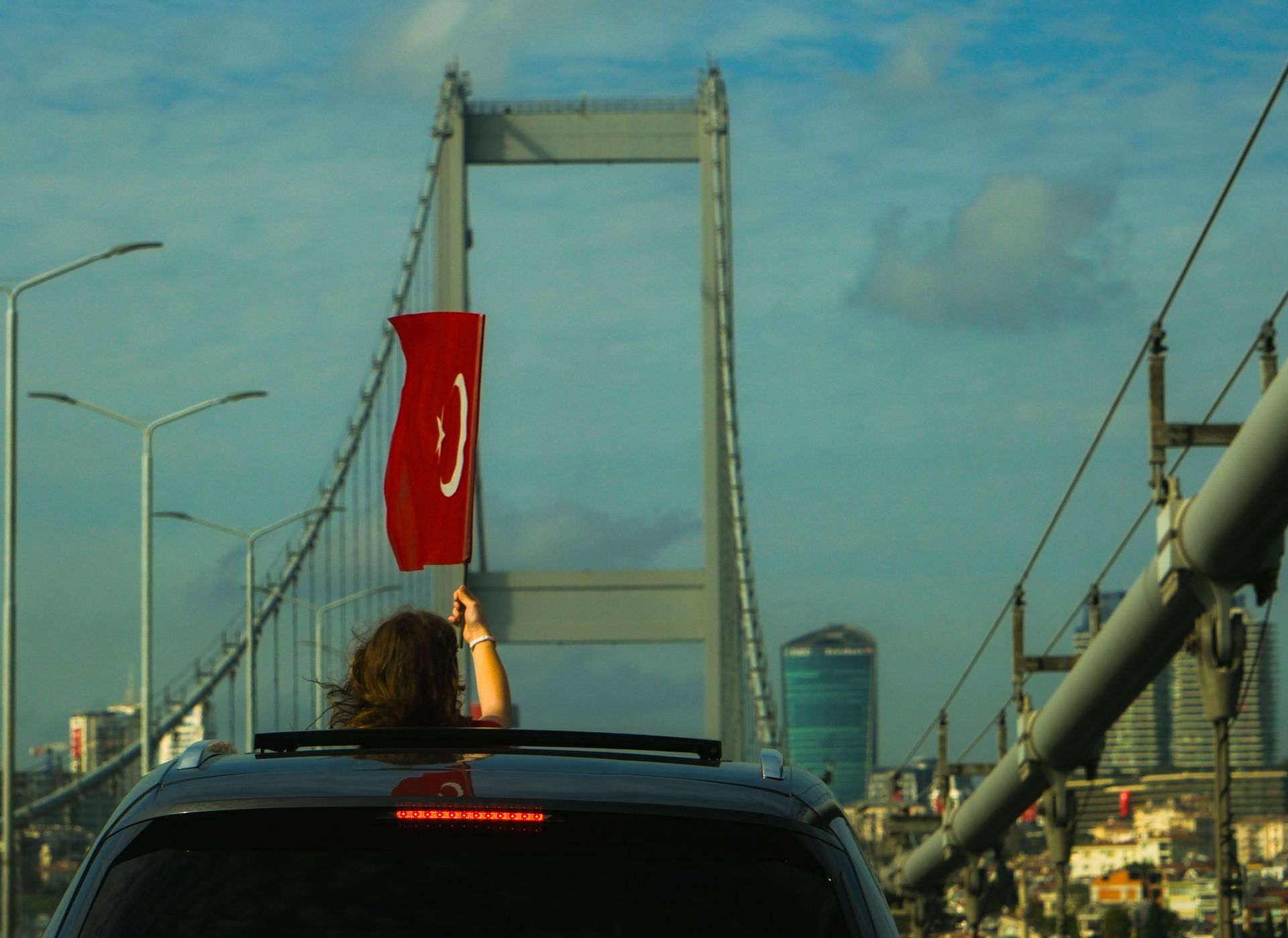 A woman waves the Turkish flag from a car on a bridge in Istanbul, showcasing urban life.