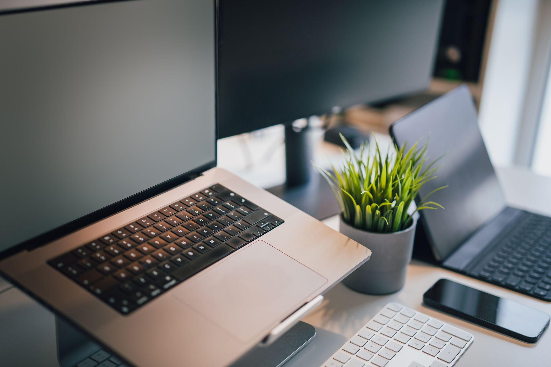A sleek office workspace featuring a laptop, smartphone, keyboard, and potted plant for productivity.