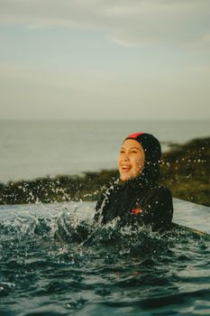 A smiling woman in swimwear enjoys splashing in a seaside swimming pool.