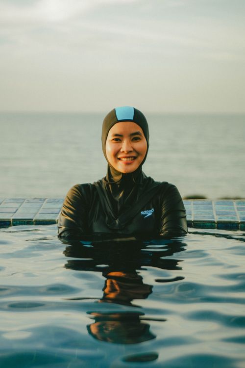 Free A woman in a swim cap smiles in a swimming pool with the sea in the background. Stock Photo