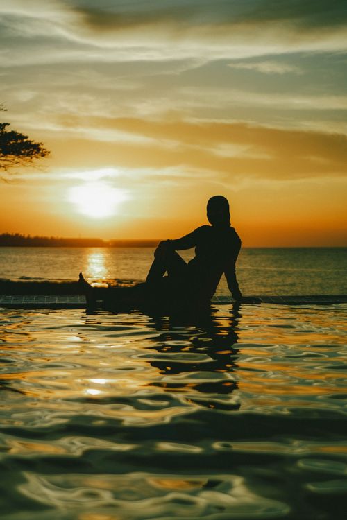 Free Silhouette of a person sitting by the sea during a beautiful sunset, creating a tranquil scene. Stock Photo
