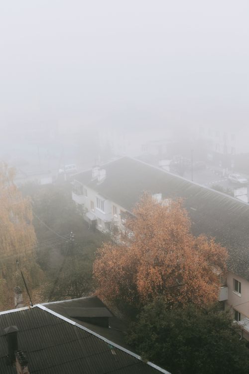 Free Aerial view of fog-covered town rooftops and autumn trees creating a serene atmosphere. Stock Photo