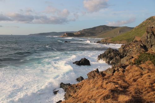 Free Breathtaking view of waves crashing against rocky coastline under a warm sunset sky. Stock Photo