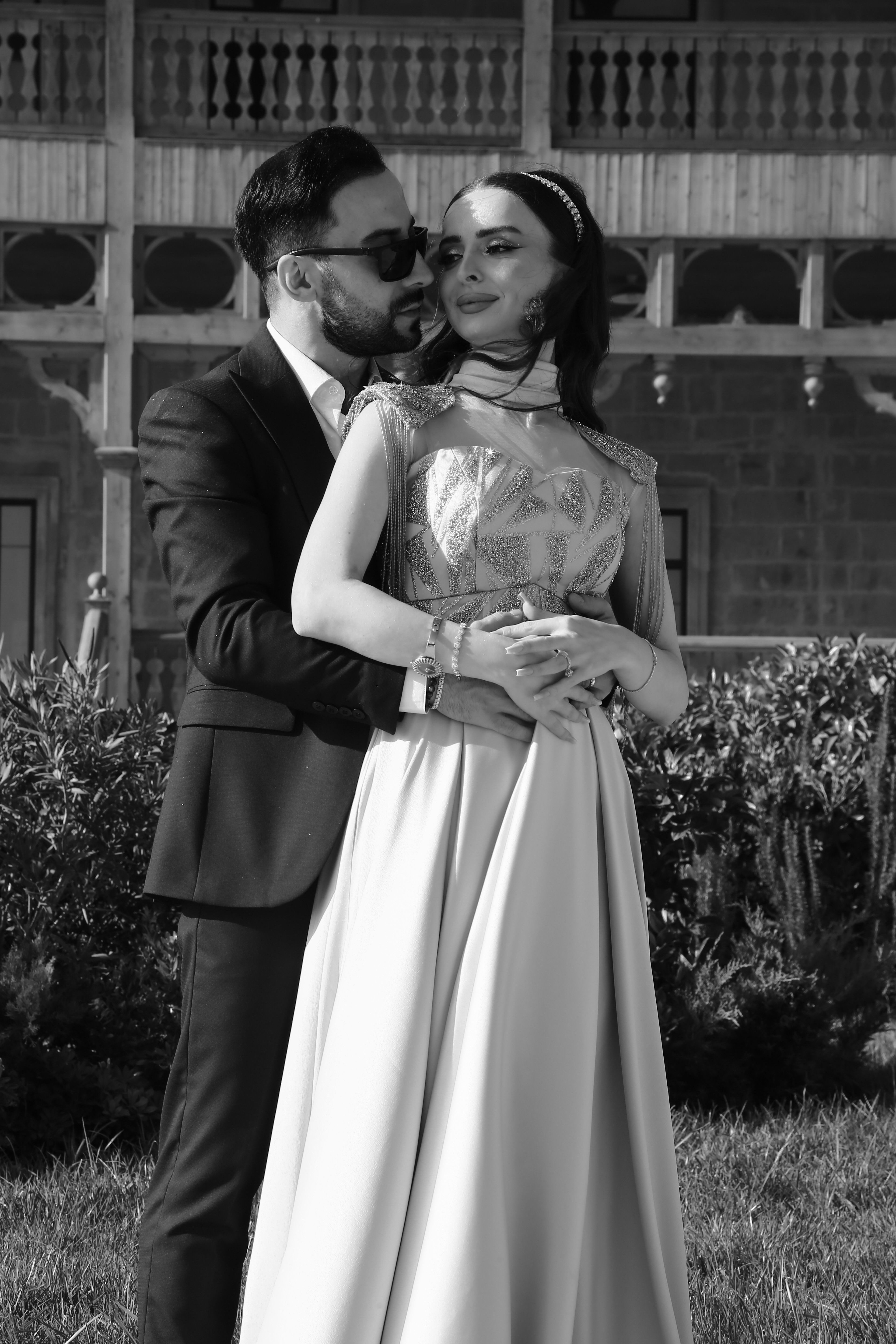 A black and white photo of an elegant couple embracing at an outdoor wedding.