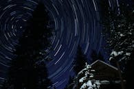在白雪皑皑的森林和小屋上空，长时间曝光的星迹旋转，展现了冬季夜空的美丽