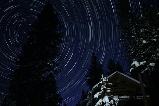 在白雪皑皑的森林和小屋上空，长时间曝光的星迹旋转，展现了冬季夜空的美丽