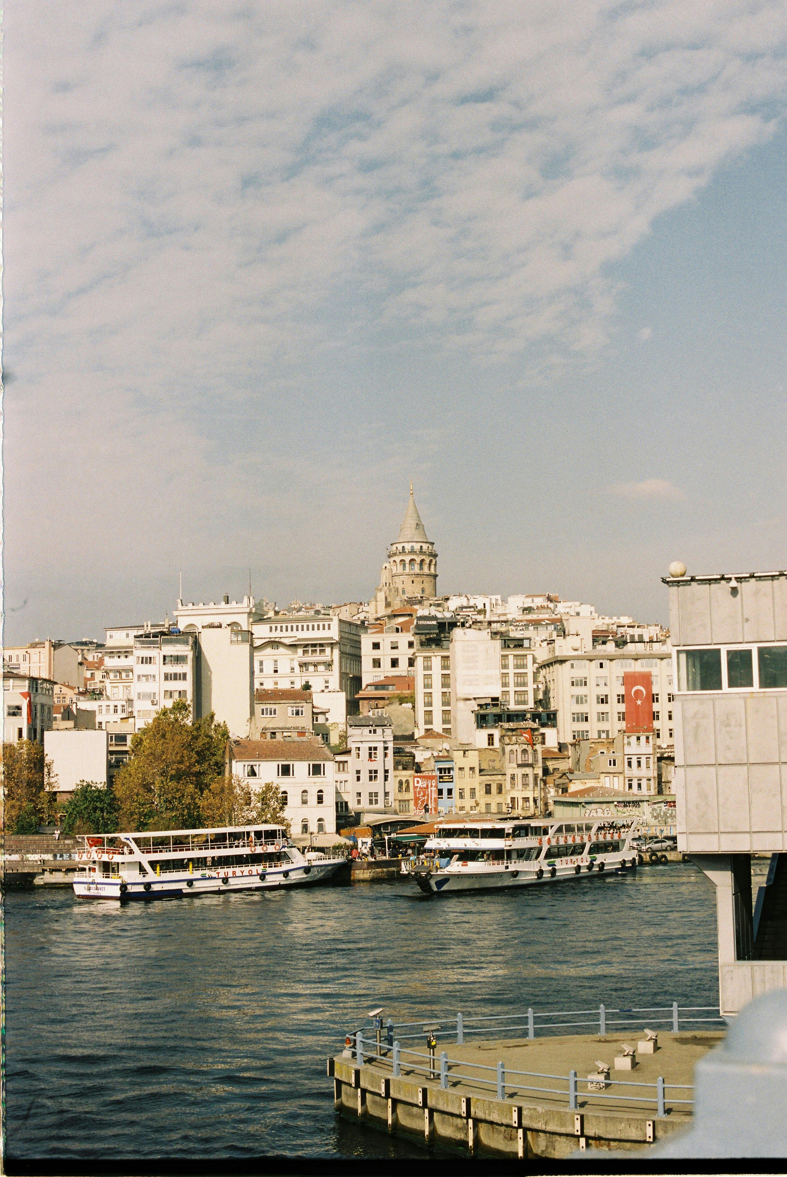 Capture of Galata Tower overlooking the bustling Istanbul waterfront with ferries and urban landscape.