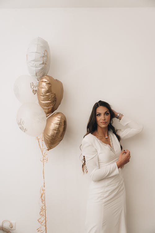 Woman in a White Dress Next to Heart Shaped Balloons