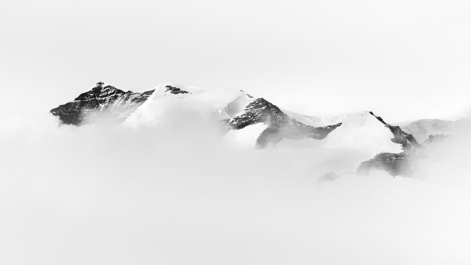Captivating black and white image of mountain peaks enveloped in fog, showcasing nature's beauty.