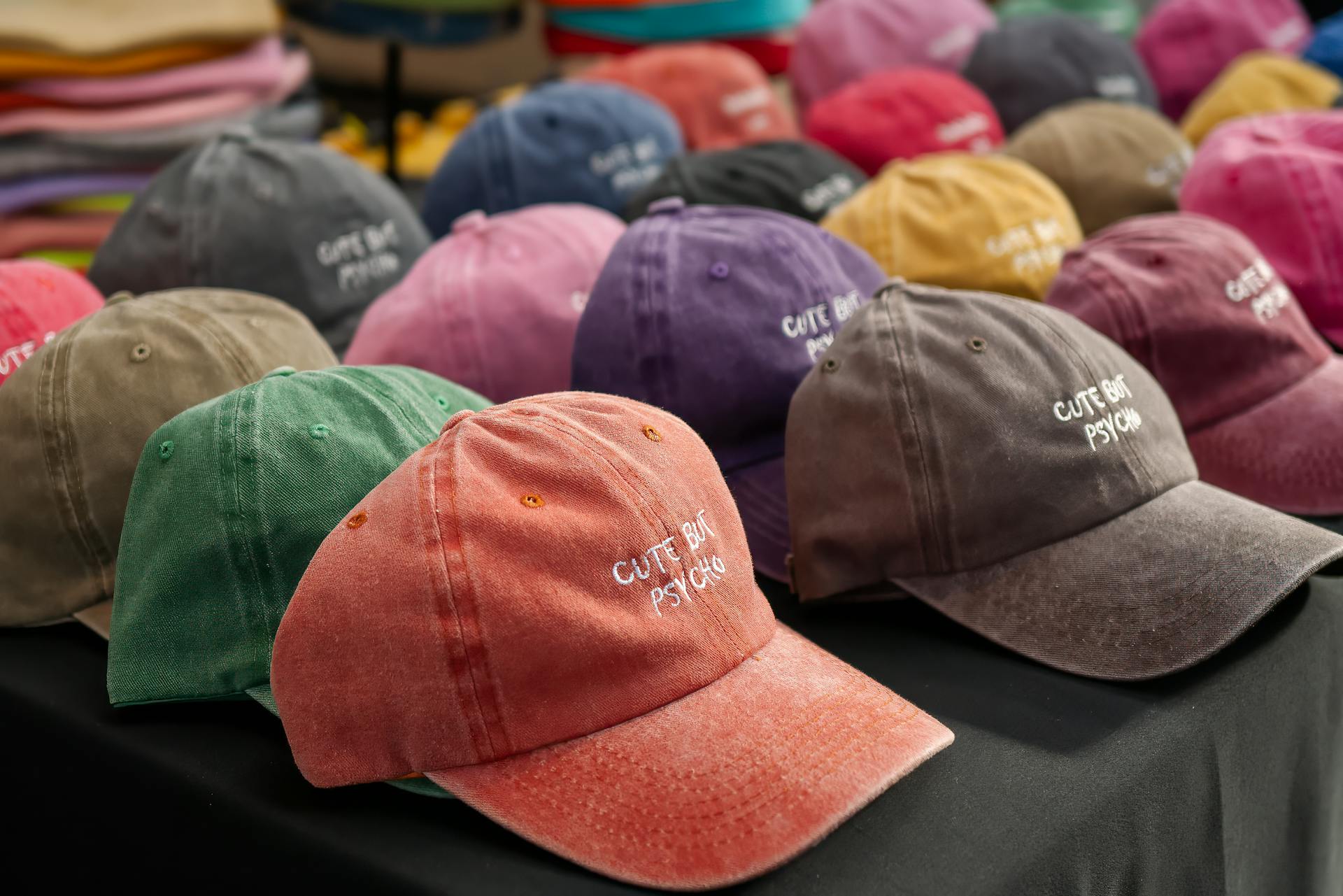 Close-up of colorful baseball caps with embroidered text at an outdoor market in England.