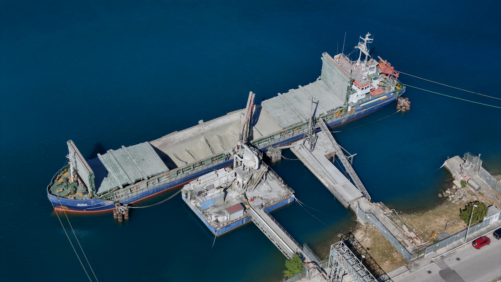 An aerial view of a cargo ship docked at an industrial loading facility, showcasing maritime transportation.