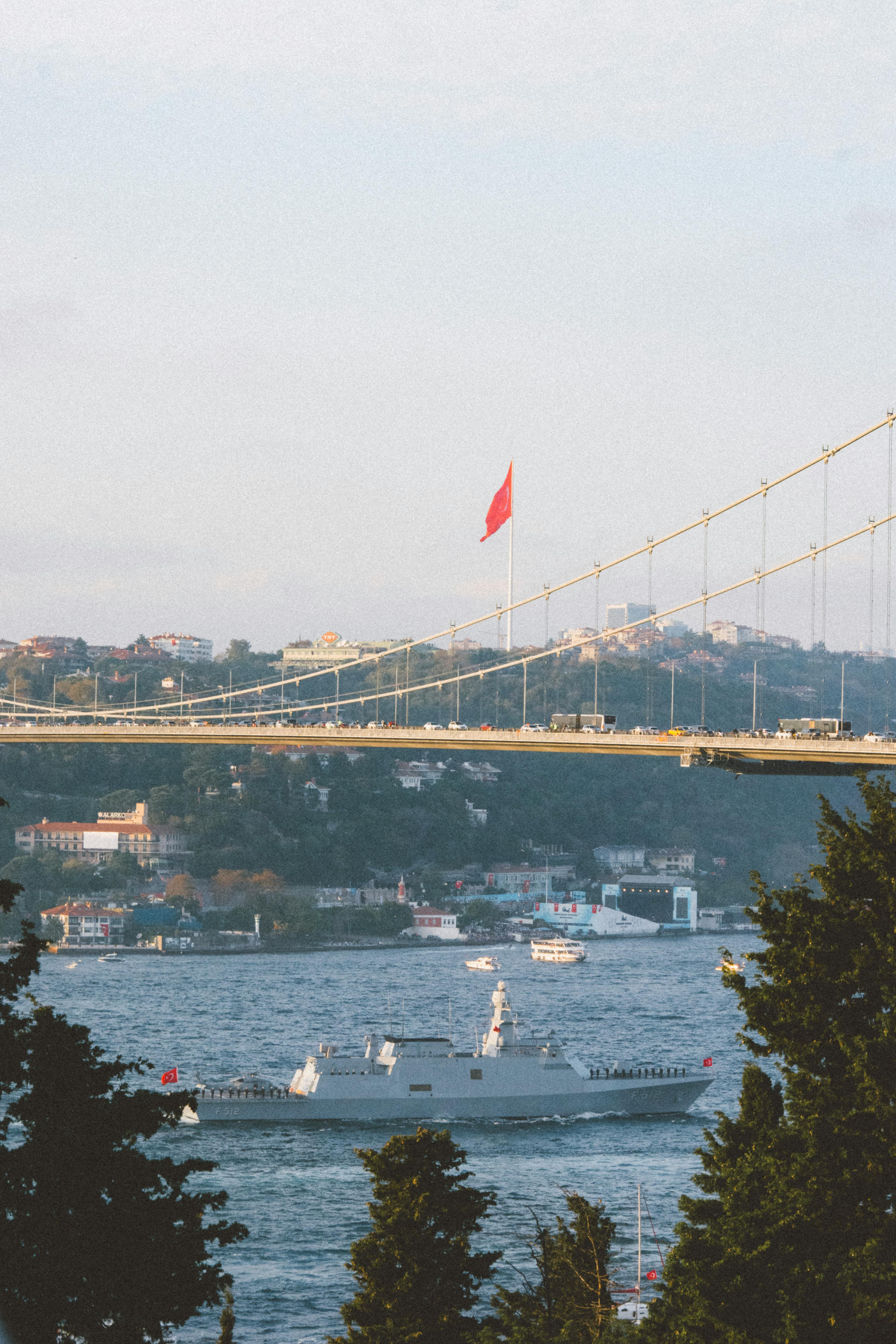 View of the Bosphorus Bridge and warship in Istanbul, with Turkish flag waving over the strait.