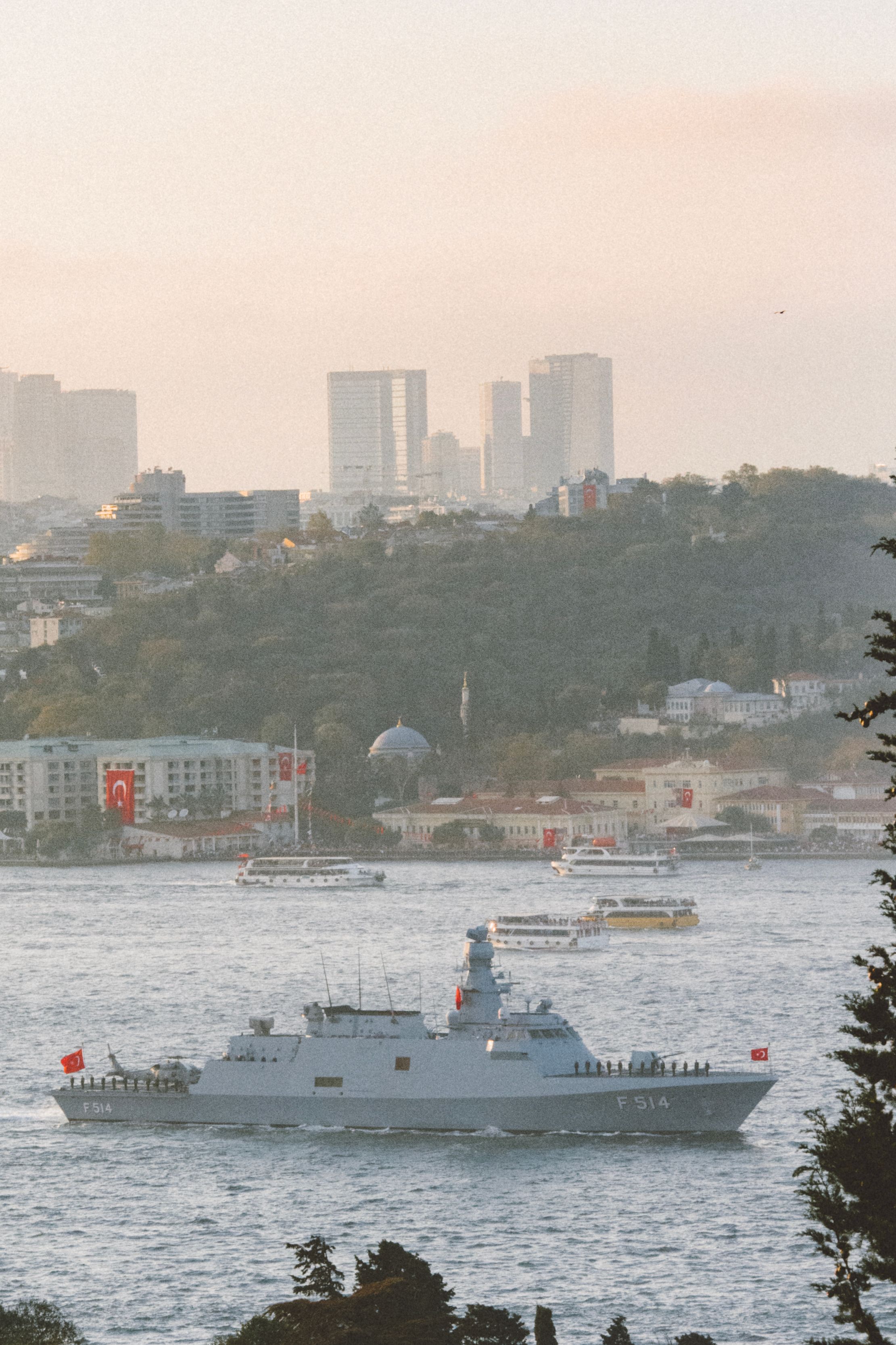 A military vessel cruises through Istanbul's Bosphorus with cityscape backdrop.