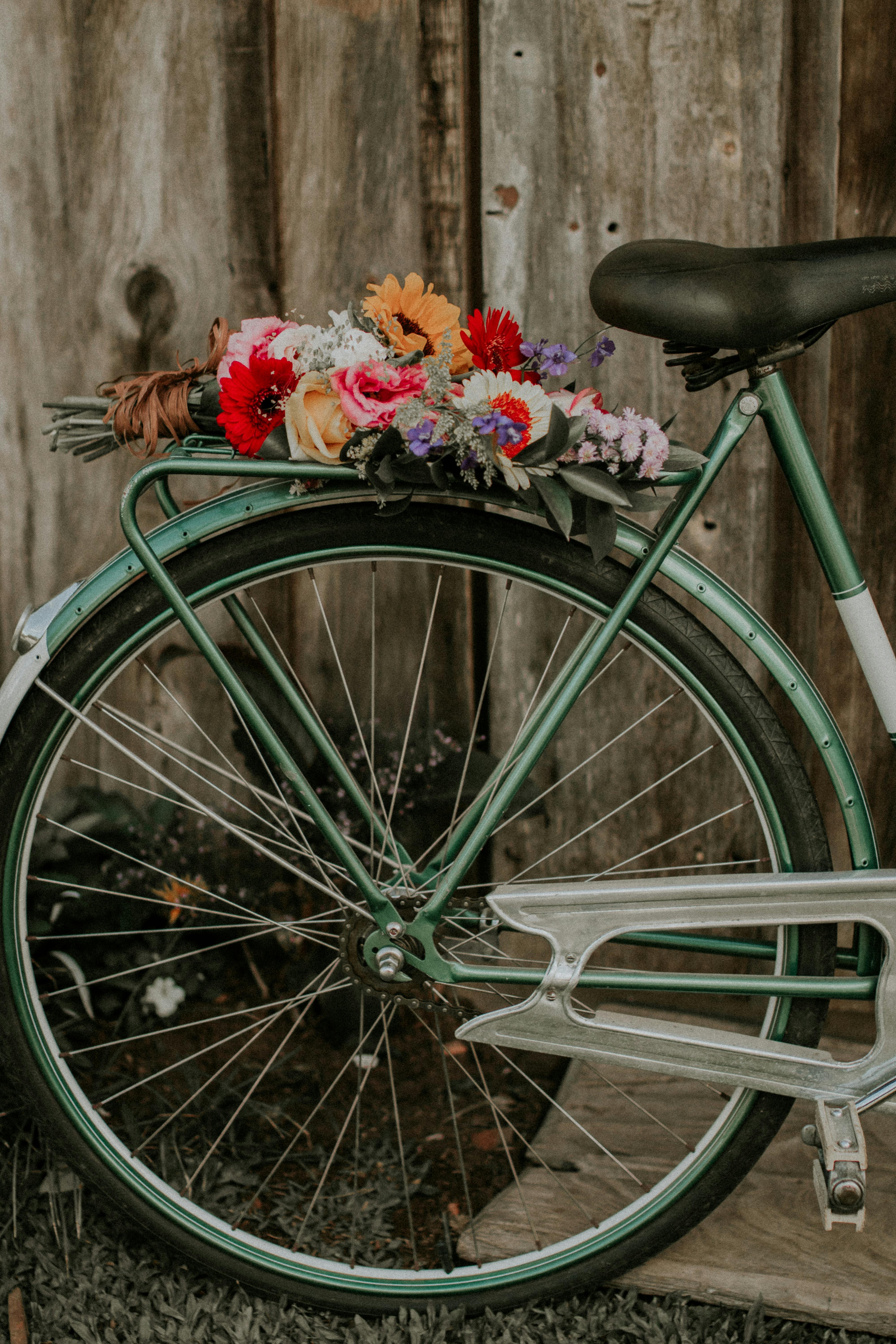 Green vintage bicycle adorned with a vibrant bouquet of flowers against a rustic wooden background.
