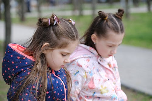Emotional scene of two adorable girls sitting pensively on a bench, expressing sadness and guilt. The introspective mood of remorseful children, showcasing their emotional connections and ...